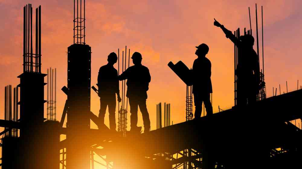 Silhouette of Engineer and worker on building site, construction site at sunset in evening time.