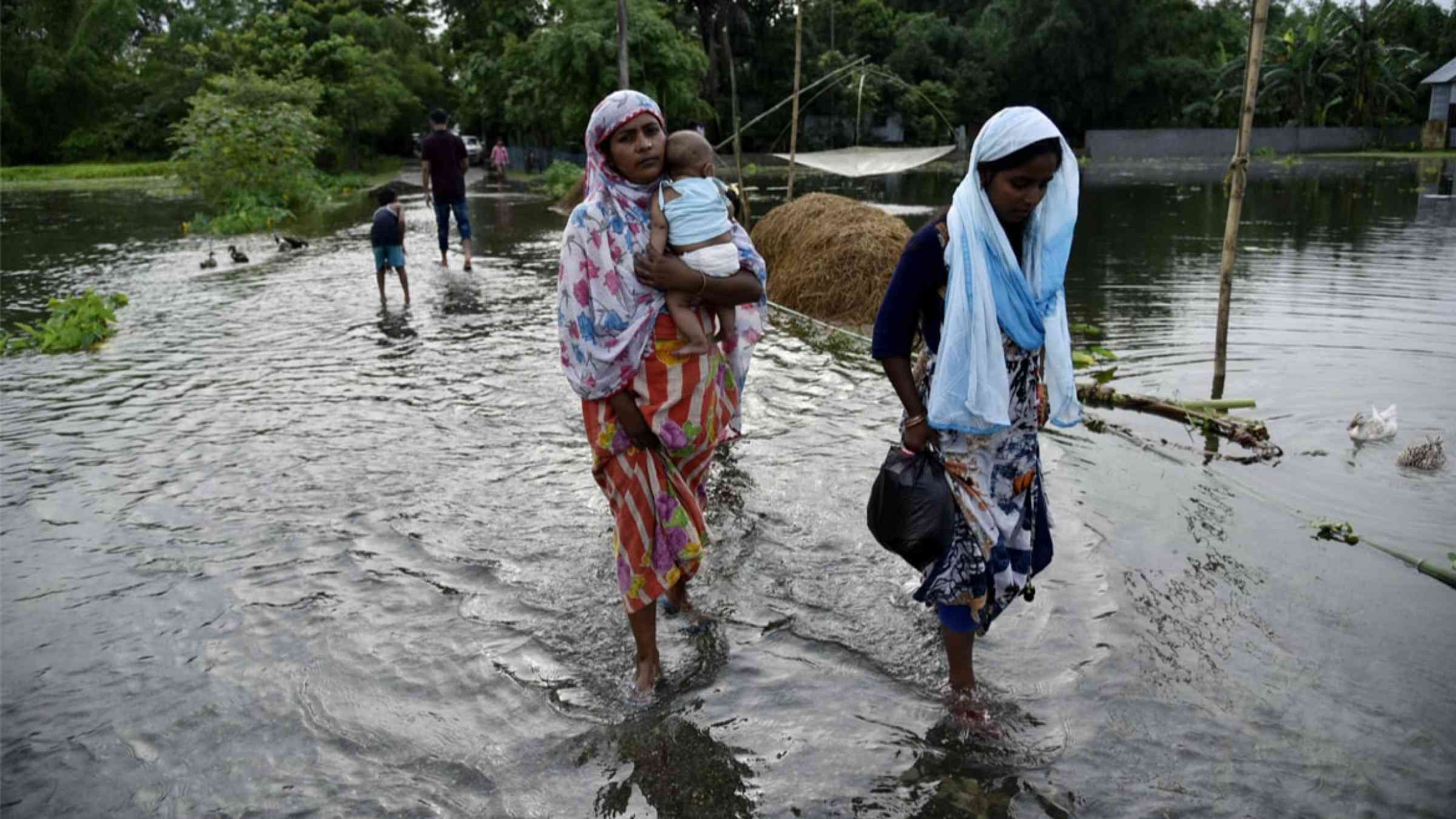 People wade through a flooded road in Assam, India (2019)