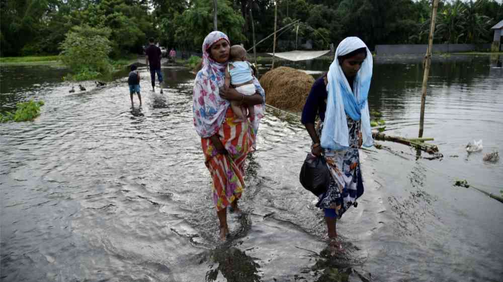 People wade through a flooded road in Assam, India (2019)