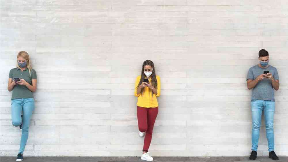 Young people wearing face mask using mobile phone keeping social distance