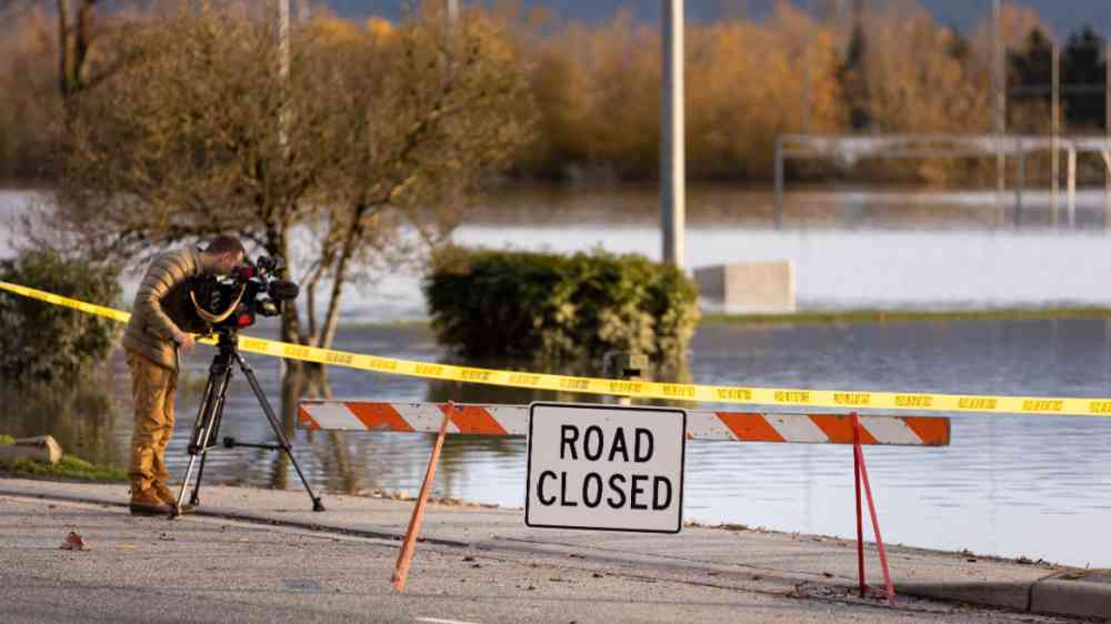 Journalist filming floods near a closed road signs due to infrastructure damage caused by heavy rain in the Fraser Valley, Canada in 2021