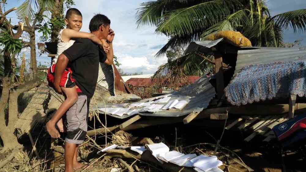 Father carrying daughter on his back seeking shelter after the destruction of their home by a typhoon in the Philipinnes