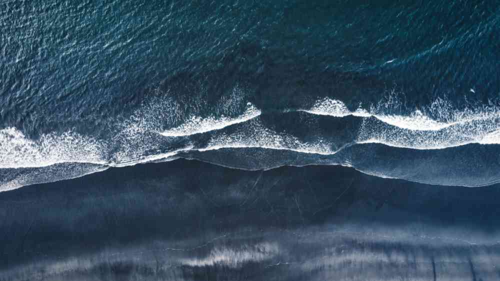 Aerial drone view of a moody atlantic ocean wave on a black sand beach during summer in Iceland