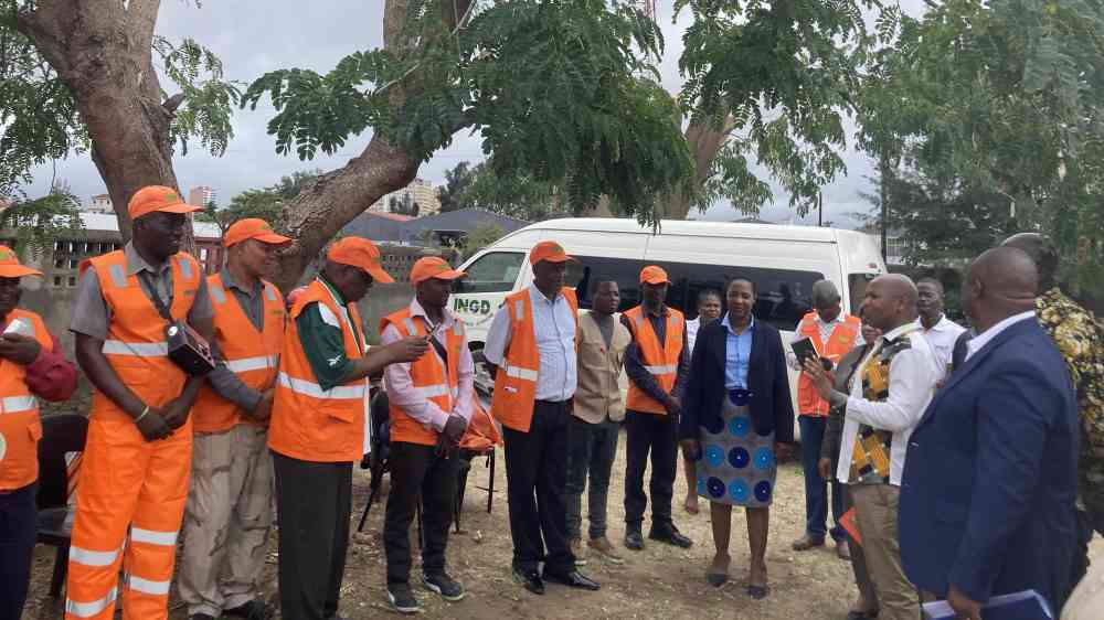 Many volunteers dressed in orange reflective jackets are gathered under a tree to discuss the dissemination of early warnings within local communities