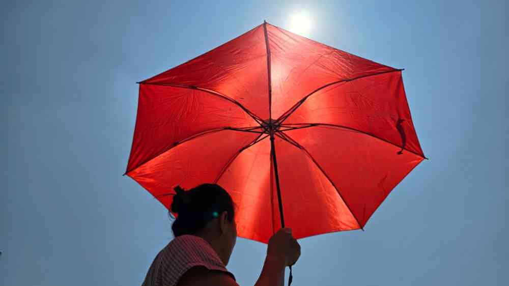 Woman with red umbrella walking outdoors in hot weather against cloudless blue sky background.