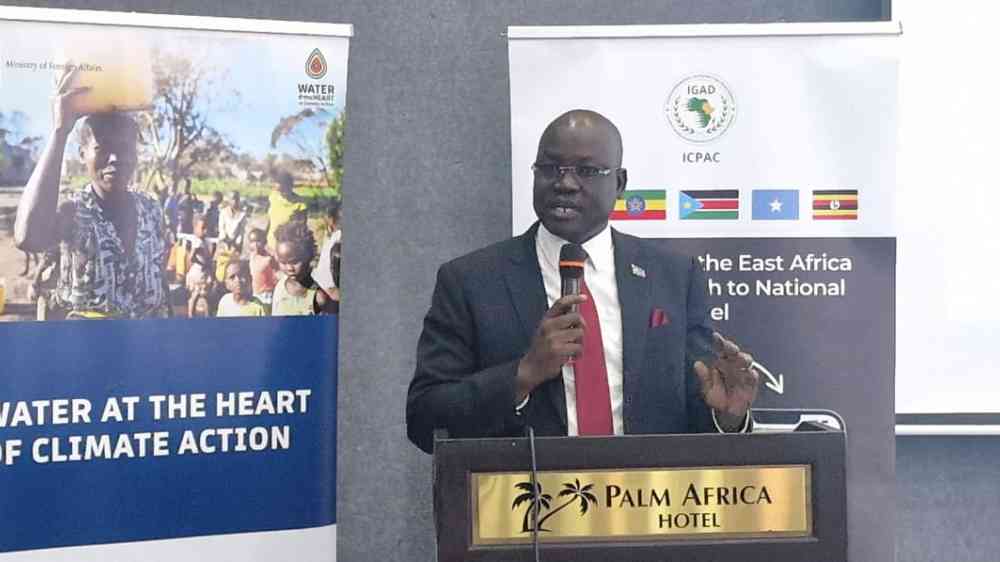 A man stands at a podium, with a microphone in hand. He is standing beside a banner for the 'Water at the Heart of Climate Action' initiative, with another banner behind him