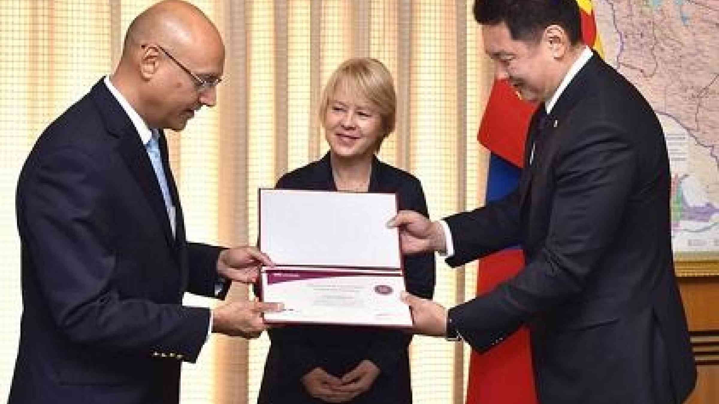 Mr. Sanjaya Bhatia (left), Head of UNISDR ONEA-GETI, receives the signing certificate of Ulaanbaatar, Darkhan and Erdenet cities  from Mr. Ukhnaa Khurelsukh, Deputy Prime Minister of Mongolia, in the presence of Ms. Beate Trankmann, UN Resident Coordinator and UNDP Resident Representative in Mongolia.