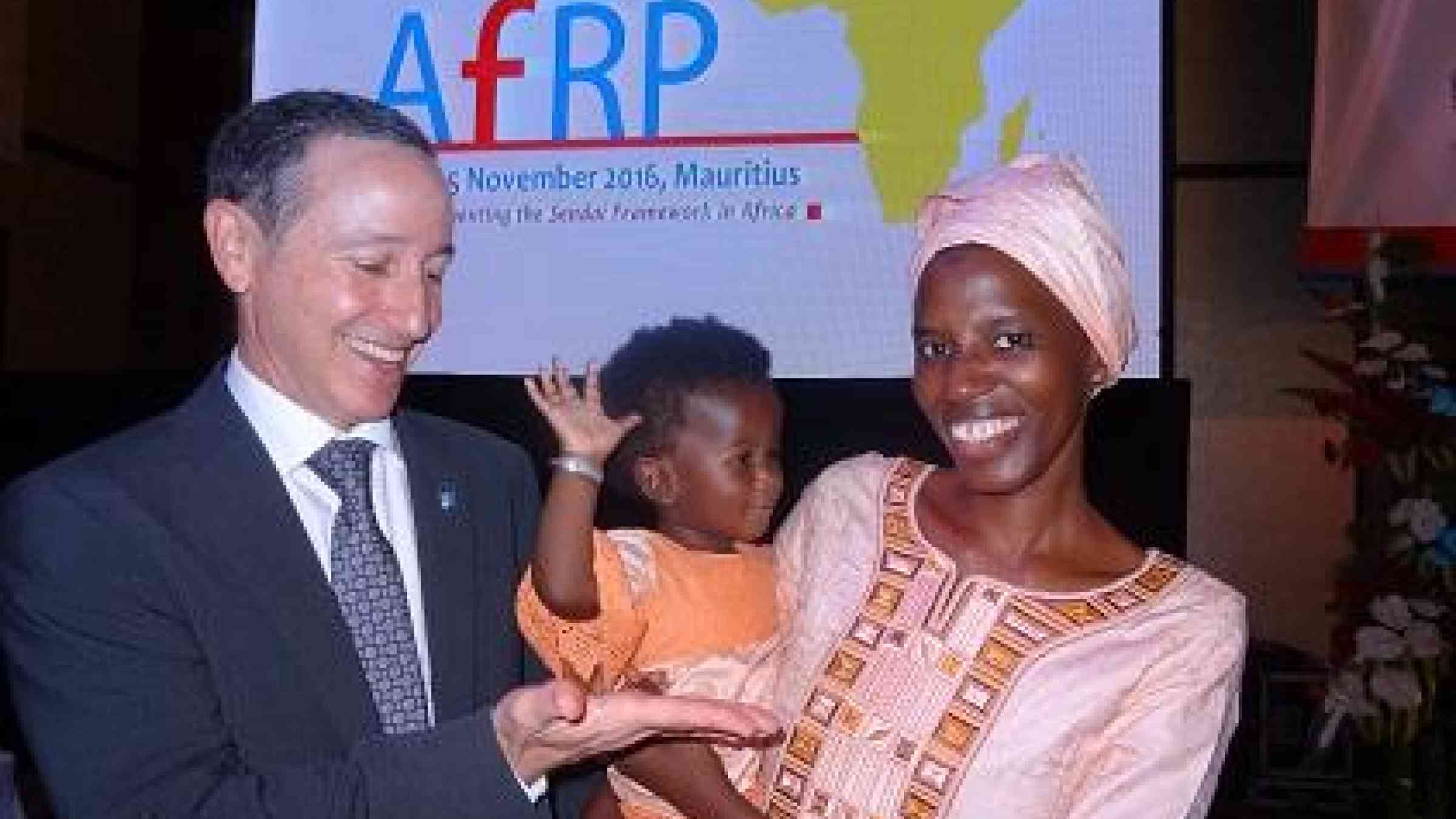 UNISDR head, Mr. Robert Glasser waits for a high-five from baby Chilal in the arms of her mother, Ms. Oumie Sissokho, Director of Operations, Gambia National Disaster Management Agency