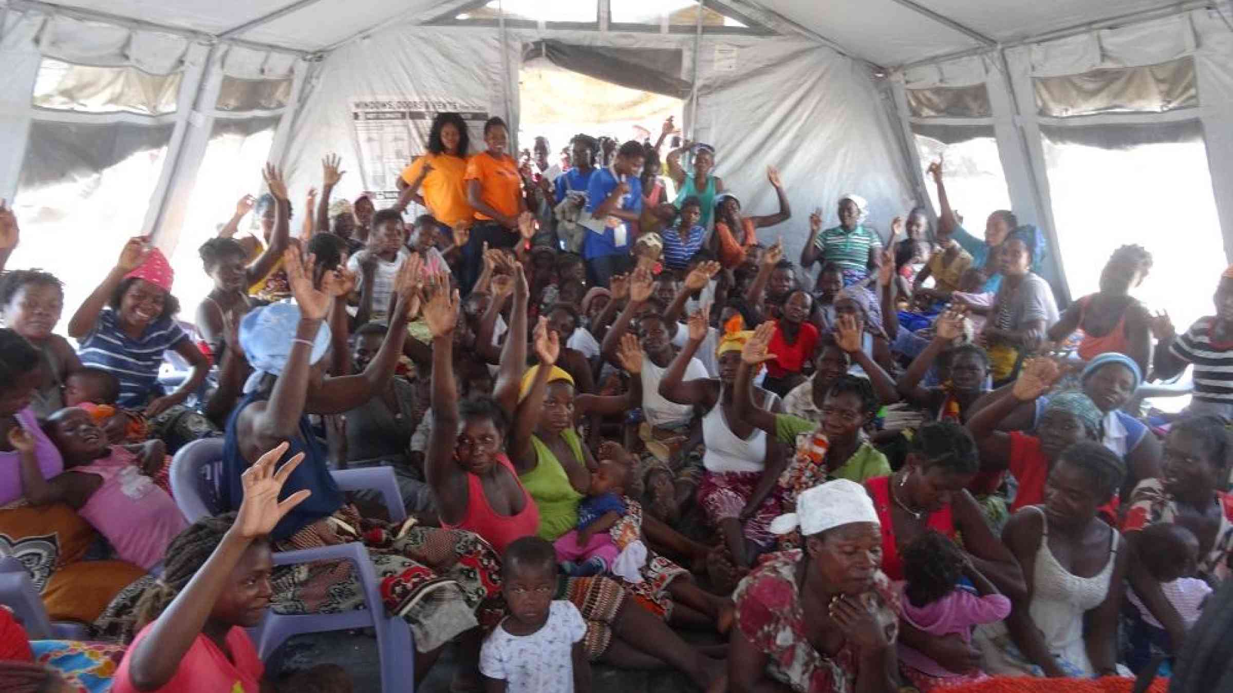 Women in a Mozambican resettlement camp raise their hands to indicate they had no warning that Cyclone Idai was about to strike
