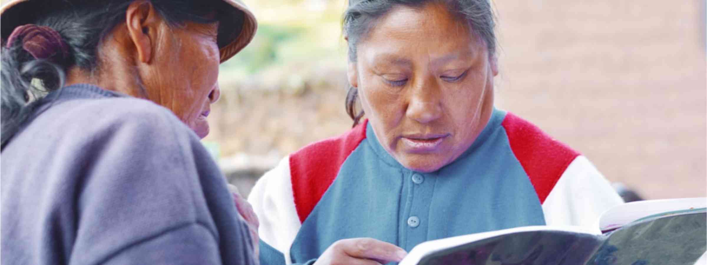 Two indigenous women looking at a book.
