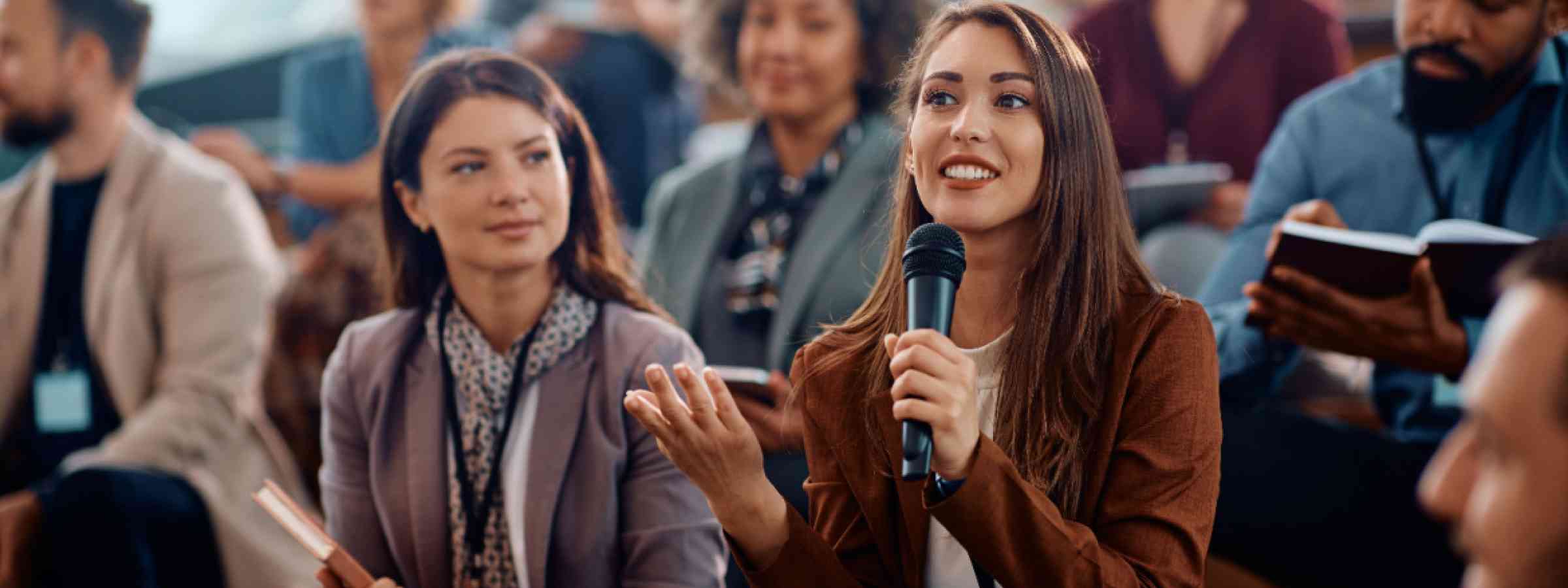 Happy female manager asking a question from the audience while participating in business seminar at convention center.