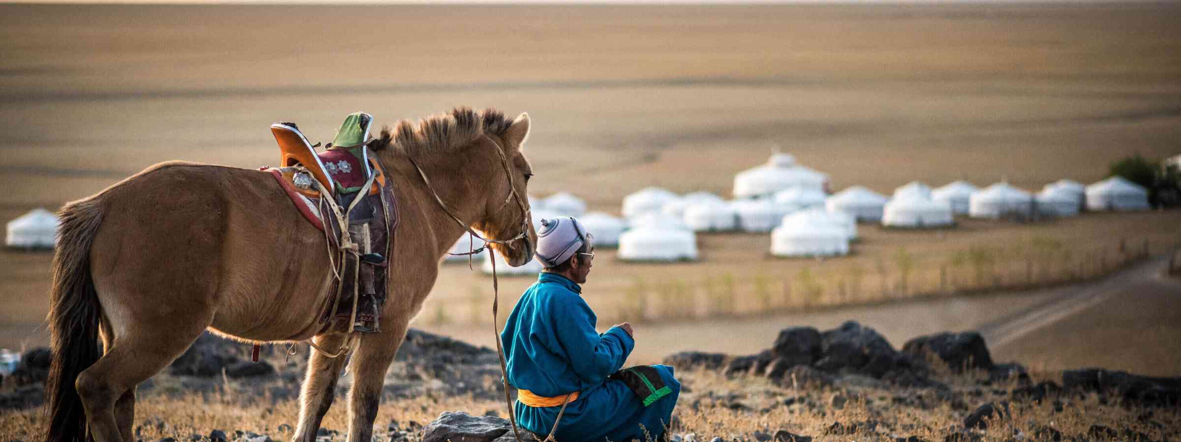 Mongolian Horse Rider In The Sunrise Morning By The Cliff Of The Mountain